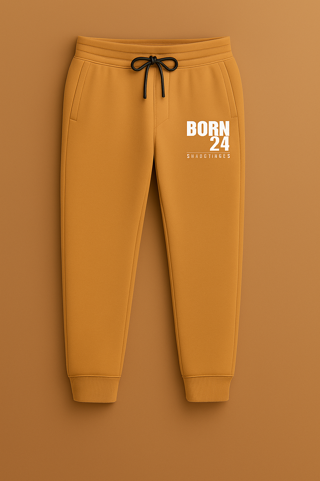 Mustard yellow sweatpants with 'BORN 24' text on a brown background